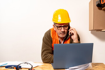 Contractor talking on cell phone while checking laptop in work office. Work organization concept, telecommunication, modern work.