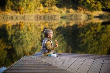 Fototapeta premium Cute European bald toddler baby in park in fall near lake