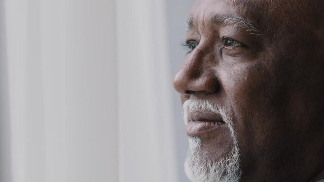 Close up pensive male old wrinkled face, 60s African bearded man deep in sad thoughts looking at window, elderly grandfather look away think about disability feel lonely. Nostalgia retired businessman