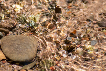 Stones in sparkling water with sunny reflections in water of a crystal clear water creek as idyllic natural background shows zen meditation, little waves and silky ripples in a healthy mountain spring