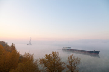 A barge ship on the river, foggy morning, pole and wires in the background. Ukraine, peace before war.