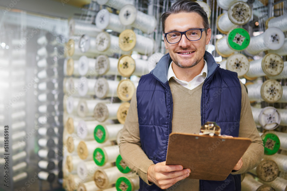 Poster Inventory is done. Portrait of a manager holding a clipboard while standing in front of wire spools on the factory floor.