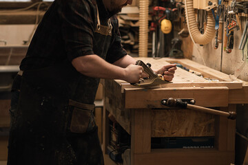 Cropped unrecognizable carpenter working with plane equipment tool on the workbench near grinder...