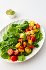 Salad with yellow and red tomatoes and spinach, top view of an oval plate with lettuce on a white background
