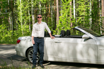 Attractive man next to a cabriolet on the background of the forest