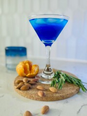 Blue curaçao cocktail on a cork wood stand with almond, orange, rosemary