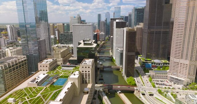 Fantastic buildings of great Chicago. Drone flying over the buildings with green areas on tops, over the river with multiple bridges on. Cloudy sky at backdrop.