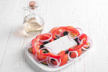 greek salad and jar with olive oil on white wooden background