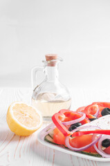 greek salad, lemon and olive oil jar on white wooden background closeup