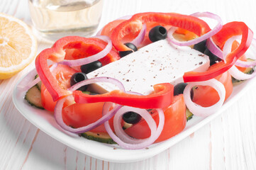 greek salad, lemon and olive oil jar on white wooden background closeup