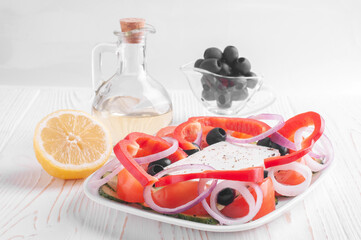 Greek salad, bowl with olive oil, bowl with olives and lemon on a white wooden background close-up