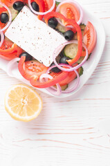 greek salad and lemon on white wooden background closeup