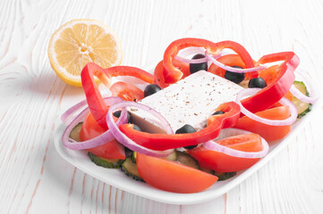 greek salad and lemon on white wooden background closeup