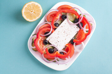 top view of greek salad and lemon on blue background