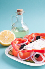 Greek salad, bowl with olive oil and lemon close-up on a blue background