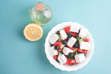 top view of greek salad, jar with olive oil and lemon on blue background