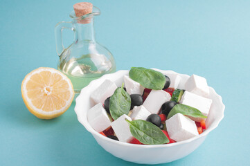 Greek salad, bowl with olive oil and lemon close-up on a blue background