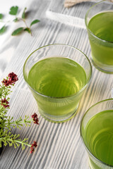 green mint jelly in a glass on a gray tray, greens and spoons nearby