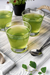 green mint jelly in a glass on a gray tray, greens and spoons nearby