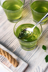 green mint jelly in a glass on a gray tray, greens and spoons nearby
