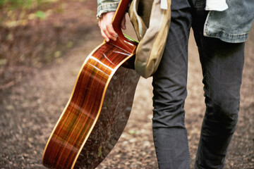 Fototapeta na wymiar Modern traveling minstrel. A cropped closeup shot of a young man carrying a guitar while walking down a forest path.