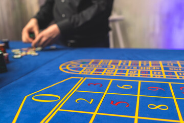Vibrant casino table with roulette in motion, with casino chips, tokens, the hand of croupier, dollar bill money and a group of gambling rich wealthy people playing bet in the background