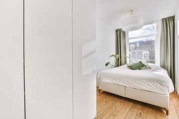 Comfortable bed and wardrobe placed in small narrow minimalist style bedroom with white walls and...