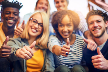 Its a thumbs up to higher education. Portrait of a group of diverse university students showing a thumbs up while sitting on the staircase on campus.