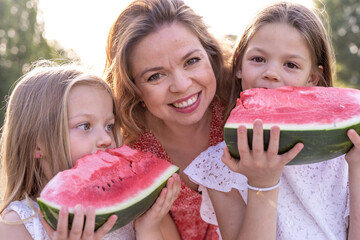 portrait of mom with cute daughters have fun while eating a slice of watermelon