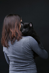 Cute black schipperke puppy posing with his woman owner on the black background