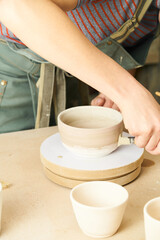 Close-up of girl painting clay mug with glaze. Woman coloring pottery in workshop with a paintbrush. Painter in green apron glazing clay pot.