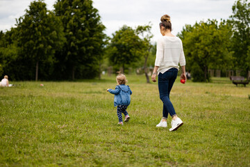 mother and daughter outdoors, having fun in park, toddler is running on the grass - obrazy, fototapety, plakaty
