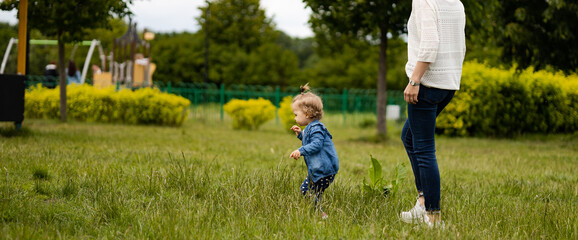 mother and daughter outdoors, having fun in park, toddler is running on the grass