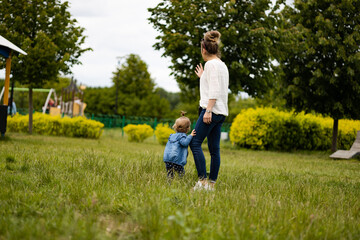 mother and daughter outdoors, having fun in park, toddler holds mother leg - obrazy, fototapety, plakaty