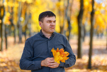 portrait of a disgruntled man, he poses with yellow leaves in an autumn park, his face has an unhappy grimace and lack of joy, a bright sunny day