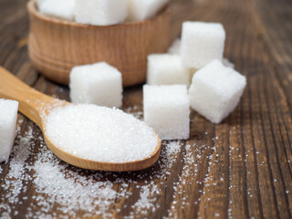 Stack of sugar cubes and granulated sugar in a wooden scoop