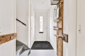 Light hallway with entrance door in apartment with minimalist wooden staircase leading upstairs in...