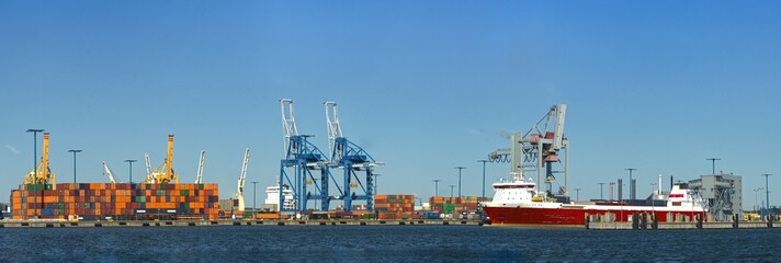 A big busy harbor with a container ship and cranes and tanks
