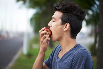 Taking a bite. A young man taking a bite of an apple while waiting for the bus.