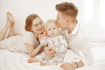 Young mother and father lay with little baby on bed, embrace and enjoy on white background. Cute relationship between parents and infant child, free copy space. Happy family and parental affection