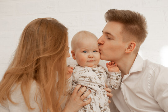Young mother and father embrace and kiss little baby, enjoy on white background. Cute relationship between parents and infant child closeup, free copy space. Happy family and parental affection