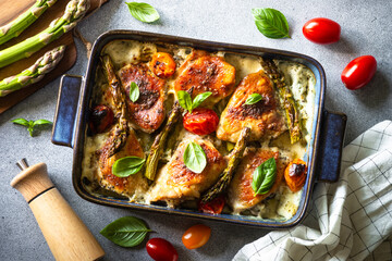 Baked chicken thighs with asparagus and tomatoes in a creamy sauce with basil. - obrazy, fototapety, plakaty