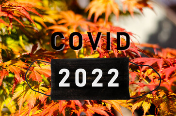Covid text with mask on autumn leafs background