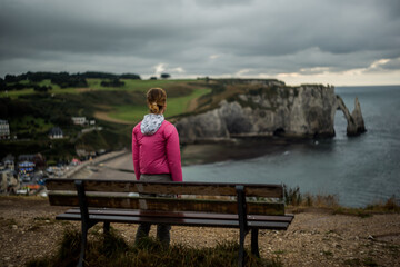 Stunning coastal view of cliffs with a woman in pink jacket reflecting by the ocean on a cloudy day...