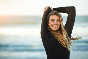 Youve gotta be limber to be a surfer. Cropped shot of an attractive young female surfer warming up on the beach.