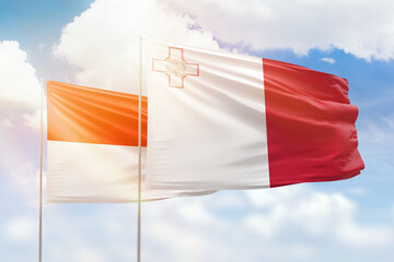 Sunny blue sky and flags of malta and indonesia