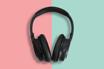 Computer headphones. Black headphones on a green-red pastel background. The concept of listening to music, creating audio, music. Computer work, abstraction and minimalist style.