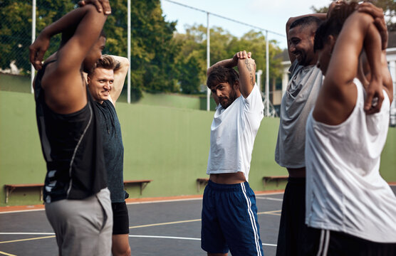 Got to warm up before we shoot some hoops. Shot of a group of sporty young men stretching their arms on a sports court.