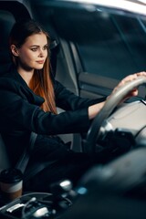 Obraz na płótnie Canvas vertical photo of a pleasant, relaxed woman sitting behind the wheel of a car with a seat belt fastened, smiling pleasantly. Photography at night