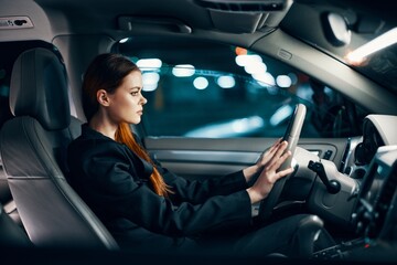 a horizontal photo from the side, at night, of a woman sitting behind the wheel in a black shirt, wearing a seat belt, looking at the road. Safe driving topics